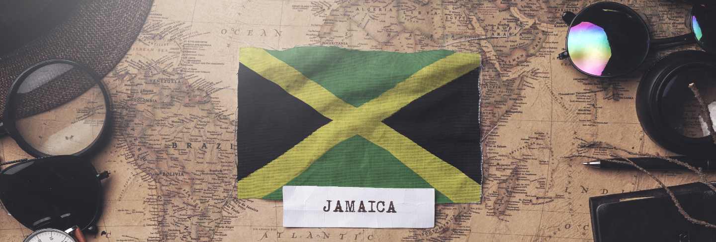 Jamaica flag between traveler's accessories on old vintage map. overhead shot

