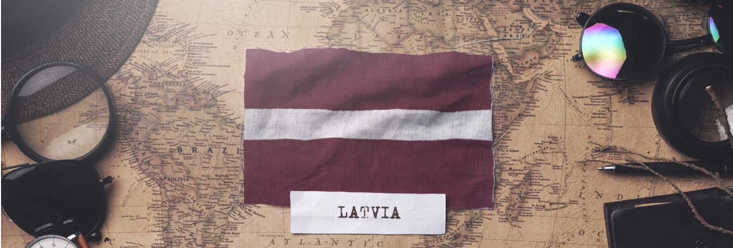 Latvia flag between traveler's accessories on old vintage map. overhead shot
