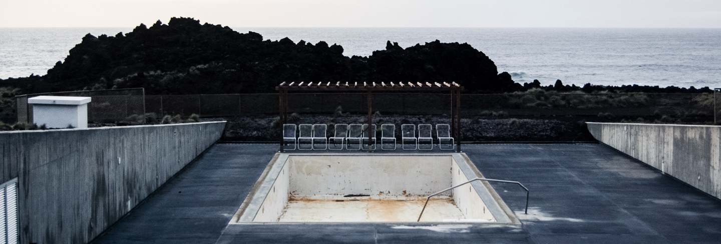 Empty pool with chairs near the cliff and a sea
