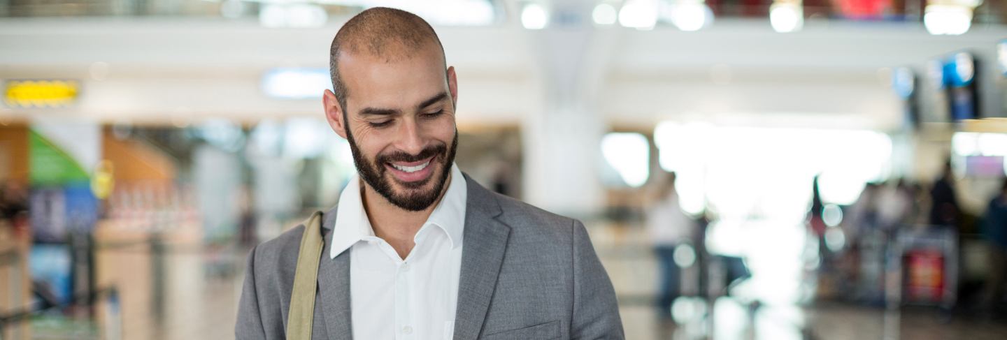 Smiling businessman holding a boarding pass and checking his mobile phone
